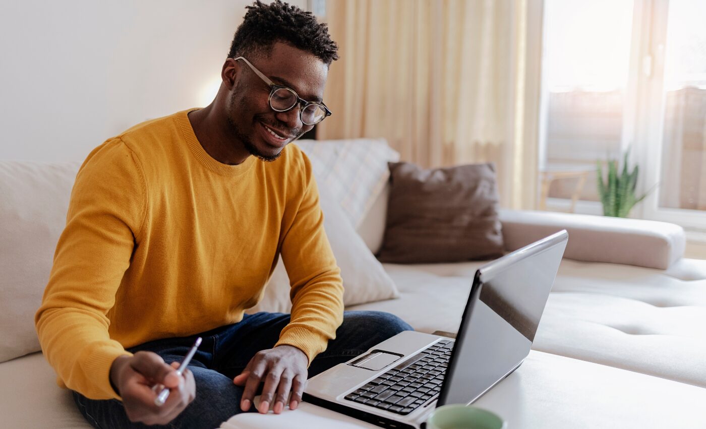 A man in a yellow jumper smiling as he works through the programme materials on his laptop